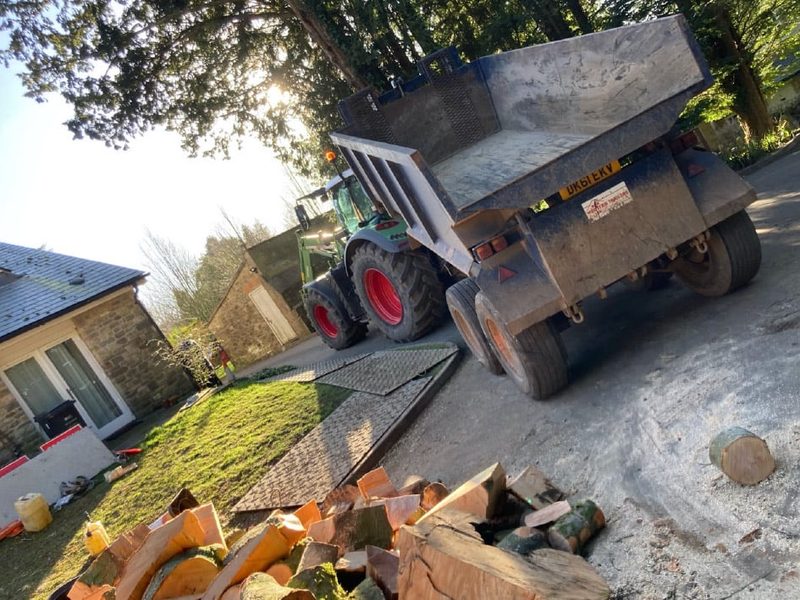 Timber split into firewood logs beside a dumper trailer on a driveway